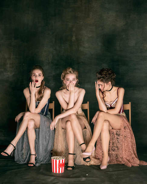 Pretty women in vintage 20s dresses. Young girls in art action sitting together and posing on wall background. - Valokuva, kuva