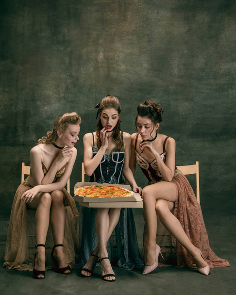 Pretty women in vintage 20s dresses. Young girls in art action sitting together and posing on wall background. - Foto, Imagem