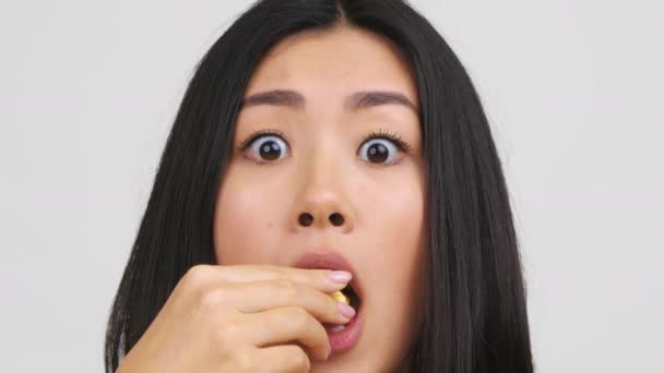Retrato de mujer china conmocionada comiendo palomitas de maíz sobre fondo blanco - Imágenes, Vídeo
