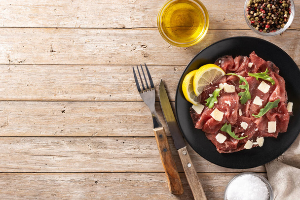 Marbled beef carpaccio on black plate and rustic wooden table. Top view. Copy space - Φωτογραφία, εικόνα