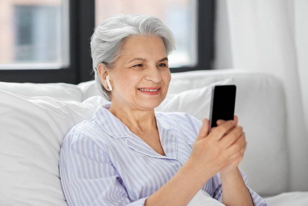 senior woman with smartphone and earphones in bed - Fotoğraf, Görsel