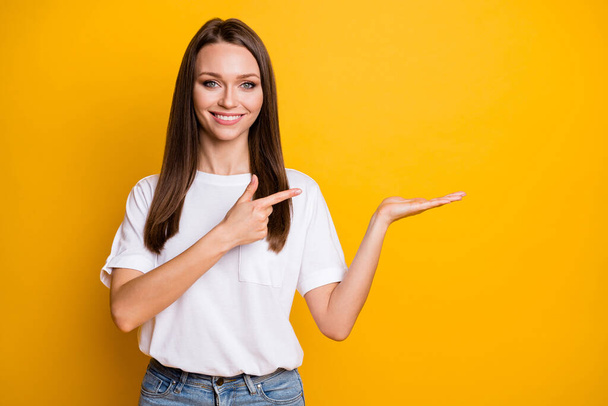 Photo portrait of woman holding blank space in hand pointing finger at it isolated on vivid yellow colored background - Φωτογραφία, εικόνα
