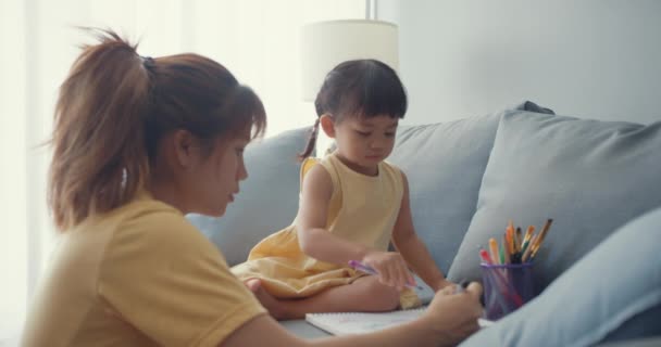 Boldog vidám ázsiai család anya tanít lány festék használata album és színes ceruzák szórakozás pihenni kanapén a nappaliban a házban. Együtt töltött idő, Társadalmi távolság, Karantén a koronavírus. - Felvétel, videó