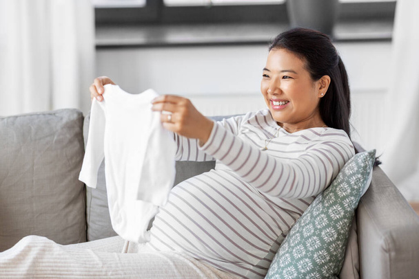 happy pregnant woman with babys bodysuit at home - Zdjęcie, obraz