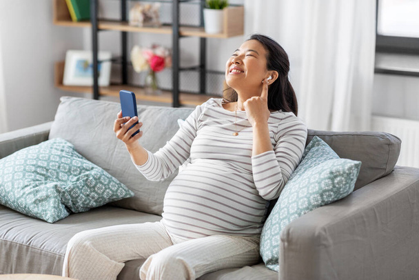 pregnant woman with phone and earphones at home - Фото, изображение