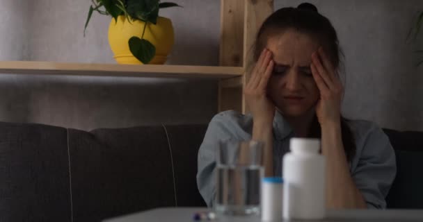 Meisje lijdt aan hoofdpijn en raakt de slapen en het gezicht aan. Pillen en water op tafel - Video