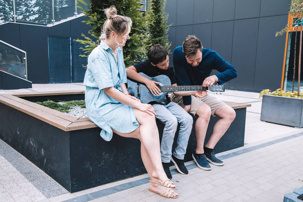 Father and son tuneguitar to play fun song to their mother on summer day in city square. Lifestyle.  - Foto, imagen