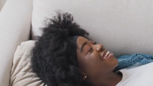 Sorridente attraente giovane studentessa afroamericana atterraggio sul cuscino godendo fine della giornata lavorativa. Millennial donna razza mista gode di fine settimana, vacanza, tanto atteso riposo piacevole a casa da solo - Filmati, video