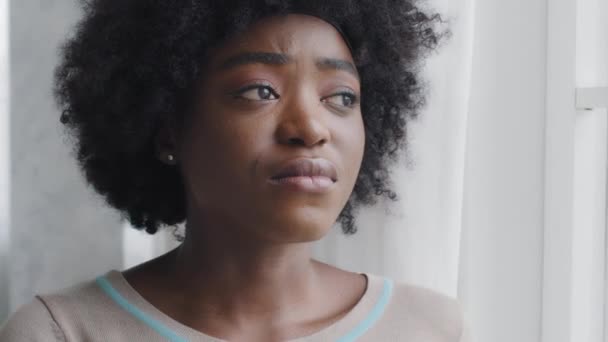 家庭の窓から外を見ている若いアフリカ系アメリカ人の憂うつな女性は、悲しいか落ち込んでいる。困難な関係最初の要求されない愛心理的感情障害の概念 - 映像、動画