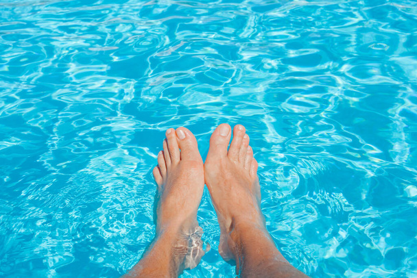 Concept vacances d'été : pieds de l'homme contre l'eau bleue de la piscine. Caustique en eau bleue. Détente, bains de soleil et joie. - Photo, image