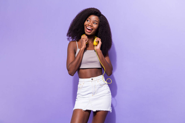 Photo of young excited black girl happy positive smile hold headphones look empty space isolated over violet color background - Fotografie, Obrázek