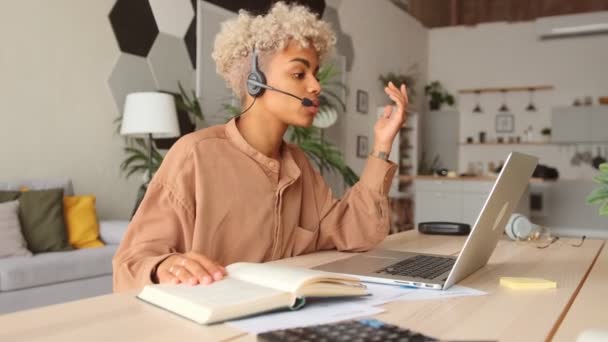 Afro businesswoman wear headset talk by conference call via laptop at home office - Filmati, video