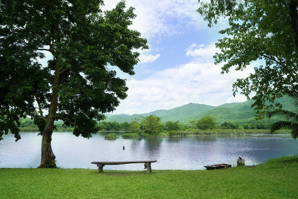 Wooden chairs are placed by the river for outdoor view with blue sky over the mountain and lake view on background. Bench on the lake for Sit and relax in a shady atmosphere amidst nature. - Photo, Image