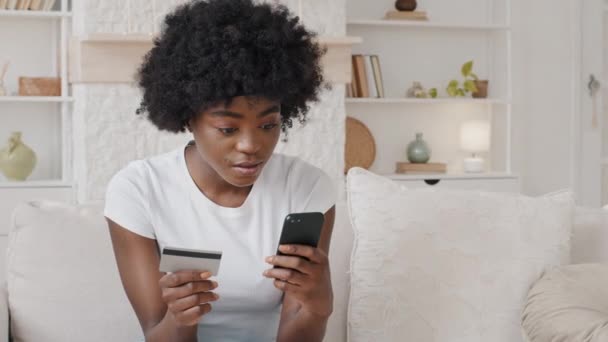 African woman holding cellphone and plastic bank card, female client entering payment information in shopping application, purchasing goods or services quickly in store. Spend money online concept - Footage, Video