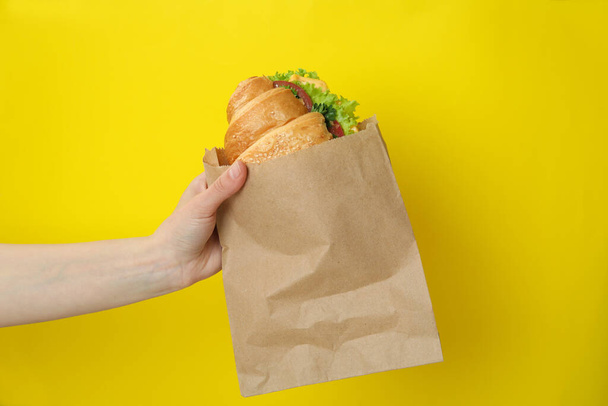Sándwich de croissant de mano femenina sobre fondo amarillo - Foto, Imagen