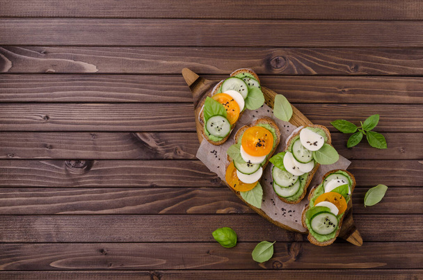 Сэндвичи с овощами, сыром и зеленым соусом на деревянном фоне. Вид сверху. - Фото, изображение