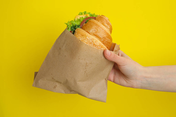 Female hand hold croissant sandwich on yellow background - Fotoğraf, Görsel