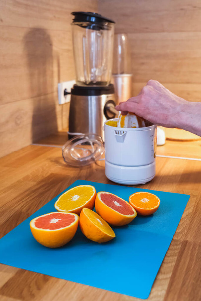 Mężczyzna wyciska sok na sokowirówkę z pokrojonych czerwonych i pomarańczowych pomarańczy w kuchni - Zdjęcie, obraz