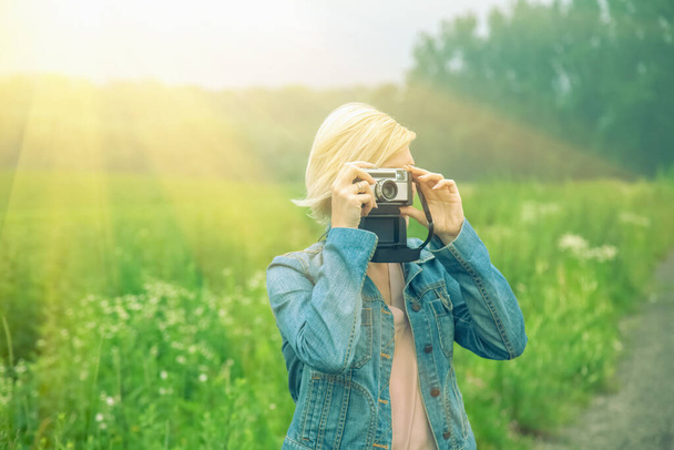 Beautiful blonde female photojournalist traveling and taking picture outdoors in sun rays  - Фото, изображение