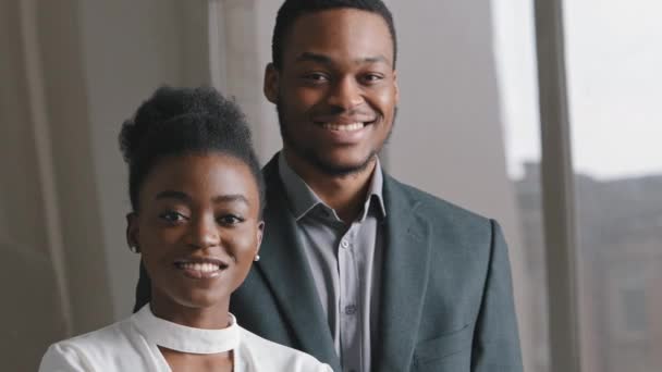 Magabiztos mosolygós pár Millenniumi afro-amerikai nő és öltönyös férfi néz kamera pózol az irodában, boldog etnikai fiatal szakmai, diákok vagy üzletemberek closeup üzleti portré - Felvétel, videó