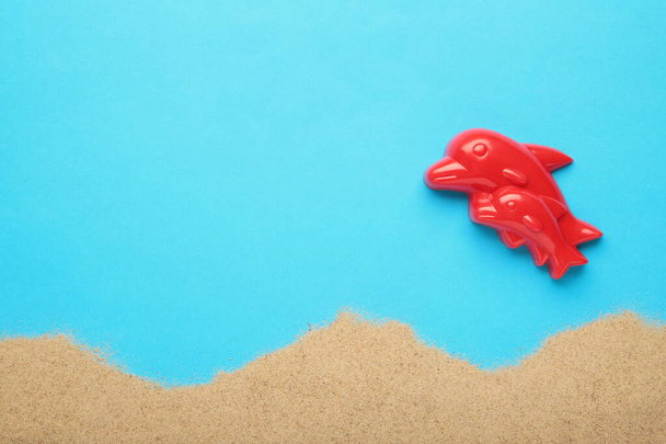Red Dolphin toy with sand on blue background. Summer composition. Top view - Fotografie, Obrázek