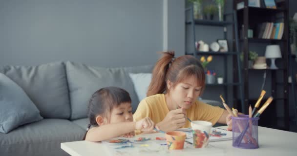Mutlu, neşeli Asya ailesi annesi küçük kıza seramik tencereyi boyamayı öğretiyor. Evdeki oturma odasındaki masada keyfine bakıyor. Birlikte zaman geçirmek, sosyal mesafe, koronavirüsü önlemek için karantina. - Video, Çekim