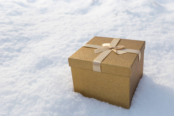 雪の弓の風景の中に金のギフトボックス。トップビュー、フラットレイアウト。ショッピングのコンセプト - 写真・画像