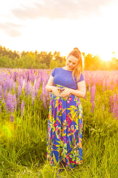 Porträt eines schwangeren Mädchens in einem blühenden Feld in der Sonne bei Sonnenuntergang - Foto, Bild
