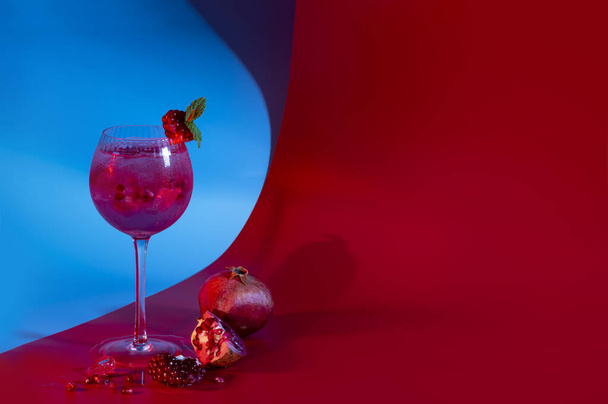 Cocktail de grenade gin tonique avec glaçons et feuilles de menthe sur fond rouge et bleu abstrait. Espace de copie neutre - Photo, image
