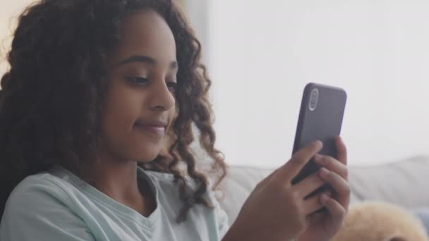 Lähikuva muotokuva teini afrikkalainen amerikkalainen tyttö verkostoituminen matkapuhelimeen, pelejä tai chattailuun ystävien kanssa verkossa - Materiaali, video