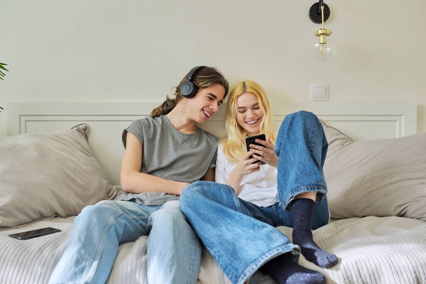 Happy laughing hipster teenagers male and female having fun using smartphone together - 写真・画像