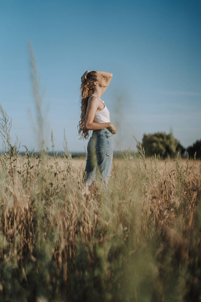 A beautiful Spanish girl holding her hair tightly with closed eyes under the sun in a wheat field - Foto, imagen