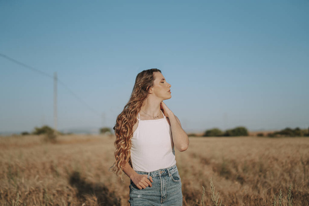 Sarışın, güzel İspanyol bir kız, açık gökyüzünün altındaki sıcak, güneşli buğday tarlasına bakıyor. - Fotoğraf, Görsel
