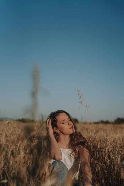 A vertical shot of a beautiful Spanish woman sitting on the ground in a wheat field under the sun - Foto, Imagen