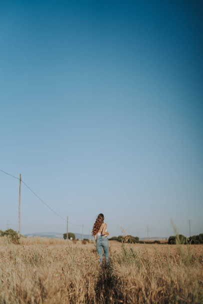 Eine schöne spanische Blondine von hinten, die unter einem klaren Himmel in einem Weizenfeld steht - Foto, Bild