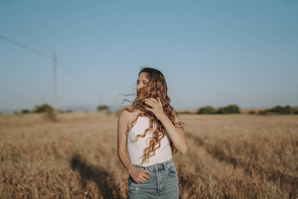 A beautiful blonde Spanish girl looking aside in a sunny wheat field with the wind blowing on her hair - Foto, Bild