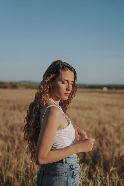 A vertical shot of a beautiful Spanish girl with curly blond locks in a wheat field on a sunny day - Photo, Image