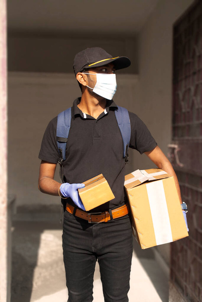Ritratto del giovane uomo di consegna che tiene la scatola di cartone sullo sfondo normale - Foto, immagini