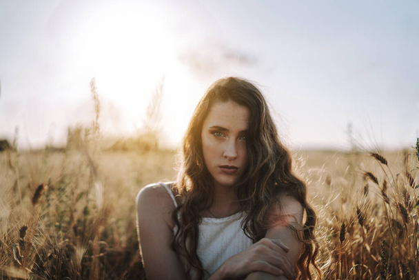 Eine hinreißende blonde Spanierin, die in einem Weizenfeld in die Kamera starrt, während die Sonne hinter ihr scheint - Foto, Bild
