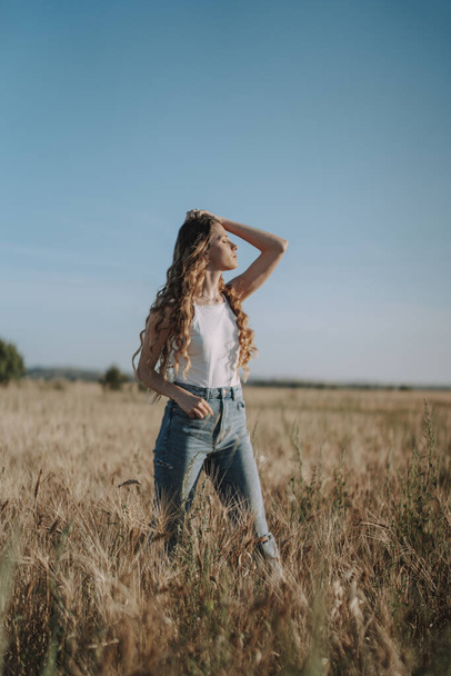 A vertical shot of a gorgeous Spanish girl running her hand through her hair under the sun in a wheat field - Фото, изображение