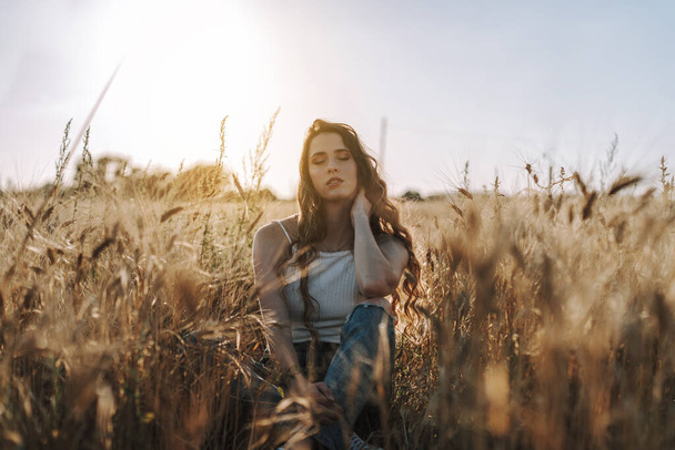 A breathtaking shot of a gorgeous Spanish woman sitting in a field with the sun shining behind her - Fotoğraf, Görsel