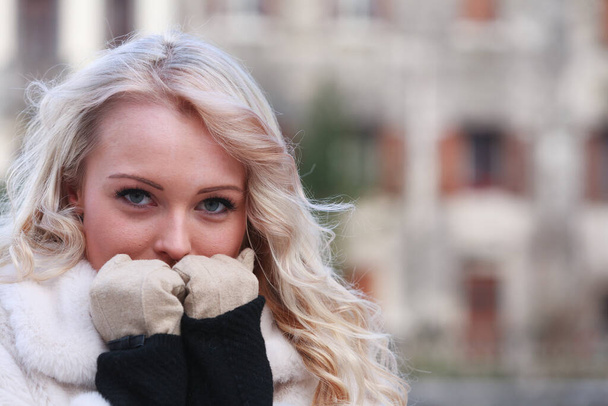 Przemyślana młoda blondynka trzymająca rękawiczki na twarzy w bliskim portrecie na świeżym powietrzu w mroźny zimowy dzień z przestrzenią do kopiowania - Zdjęcie, obraz