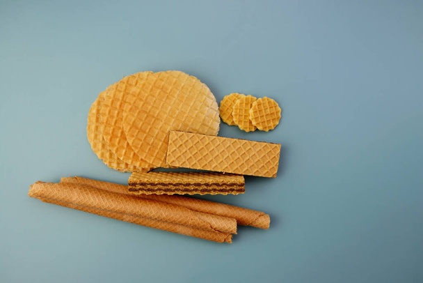 Three types of waffles on a blue background. Round waffles, filled waffles and long wafer rolls.  - Photo, Image