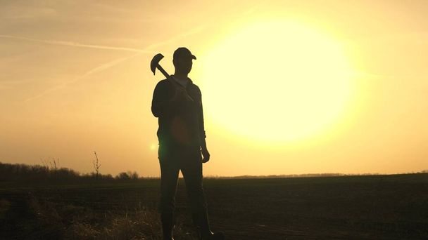 A farmer walks through the field with a shovel in rubber boots to dig the soil of the land at sunset, agriculture, land, growing vegetables, berries and fruits, planting seedlings, digging season - Photo, Image