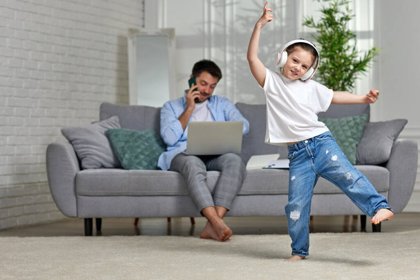 хлопчик танцює і зайнятий тато працює з ноутбуком вдома
 - Фото, зображення