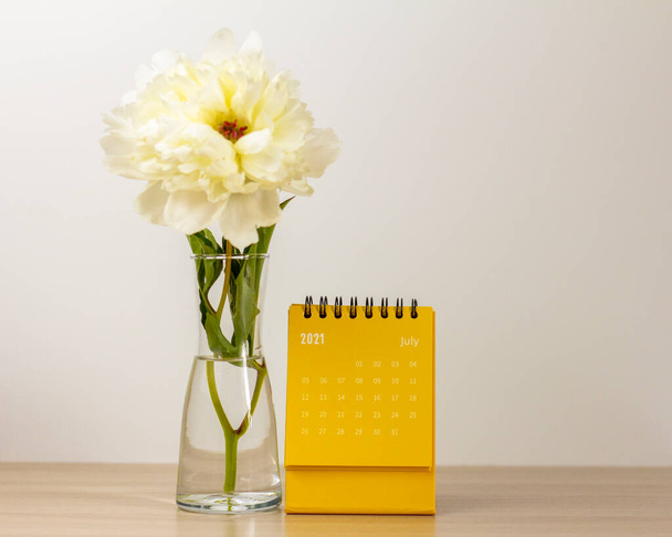 Calendar for July 2021 and peonies on the table. Desktop calendar for planning, scheduling, assigning, organizing, and managing each date - Photo, Image