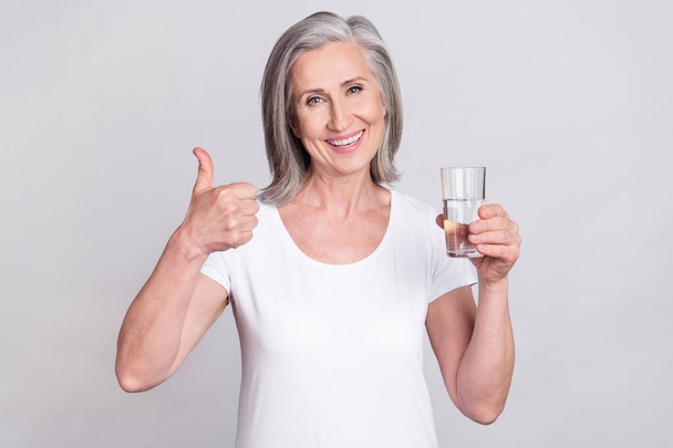 Photo of elderly woman happy positive smile show thumb-up like cool choice drink water isolated over grey color background - Foto, Imagem