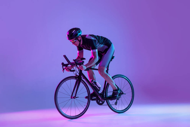 Cyclist riding a bicycle isolated against neon background - Foto, Bild