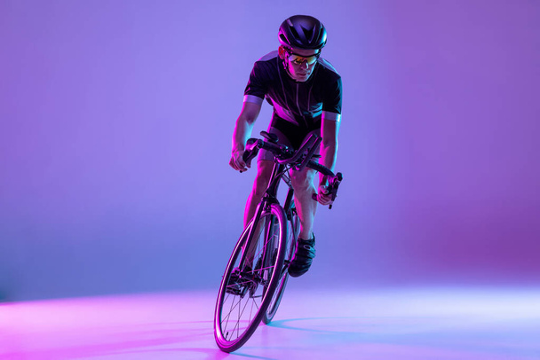 Cyclist riding a bicycle isolated against neon background - Foto, afbeelding