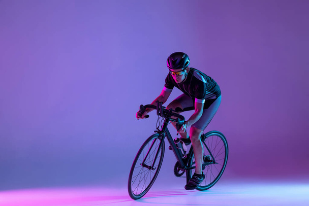 Cyclist riding a bicycle isolated against neon background - Фото, зображення